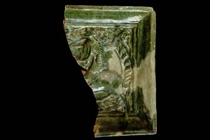 Fragment einer Halbzylinderkachel mit geschlossenem Vorsatzblatt mit Ritter beim Gestech in rundem Medaillon mit losem Tauband, grün glasiert, um 1450, Emmendingen, Hochburg
