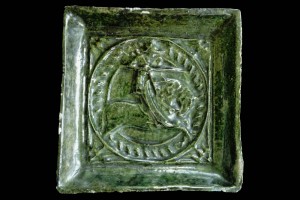 Fragment einer Halbzylinderkachel mit geschlossenem Vorsatzblatt mit Ritter beim Gestech in rundem Medaillon mit glattem Band, grün glasiert, um 1450, H. 15,5 cm, Br. 15,0 cm, Waldkirch, Elztäler Heimatmuseum
