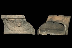 Fragment einer Gesimskachel mit geflügeltem Puttenkopf über lorbeerblattbesetztem Feston, graphitiert, zweite Hälfte 17. Jh., H. 9,5 cm, Br. 17,2 cm, Speyer, Historisches Museum der Pfalz