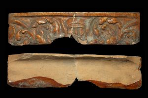 Fragment einer hängenden Kranzkachel mit einem Narrenkopf zwischen Rankenwerk, braun glasiert, Ende 16. Jh., H. 4,7 cm, Br. 19,2 cm, Speyer, Historisches Museum der Pfalz, Inv.-Nr. 11017 (1924/25)